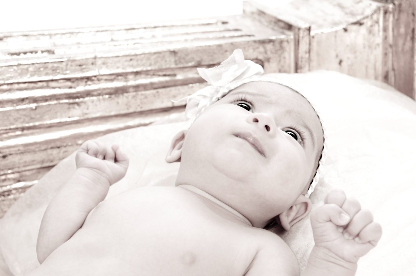 Reportajes de bebés en Capricolor Bebé acostado sobre una superficie clara, mirando hacia arriba, con una cinta en la cabeza.- Capricolor