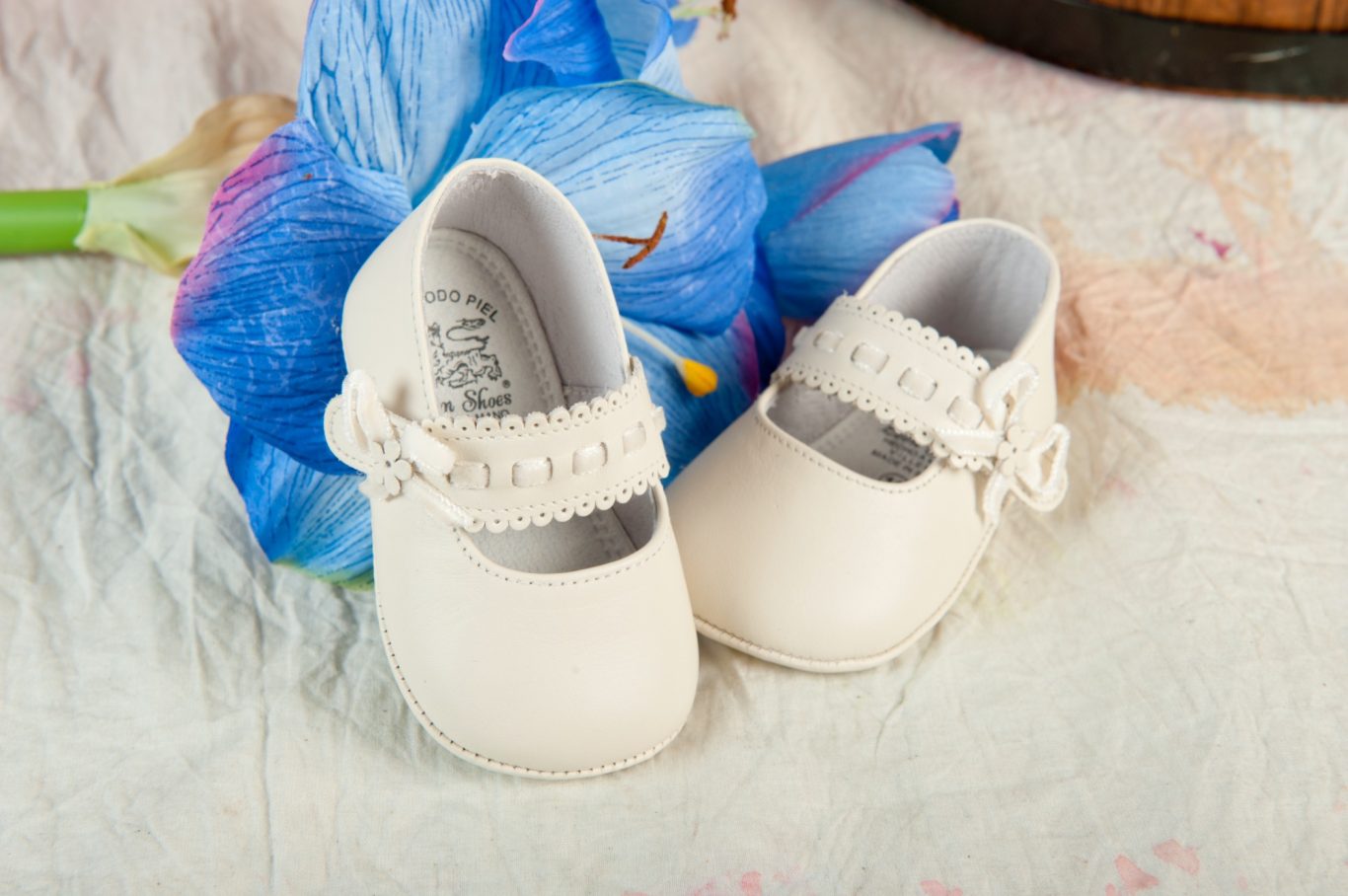 Sesiones de bebés. Zapatos de bebé blancos con una pequeña hebilla, sobre una superficie clara.- Capricolor