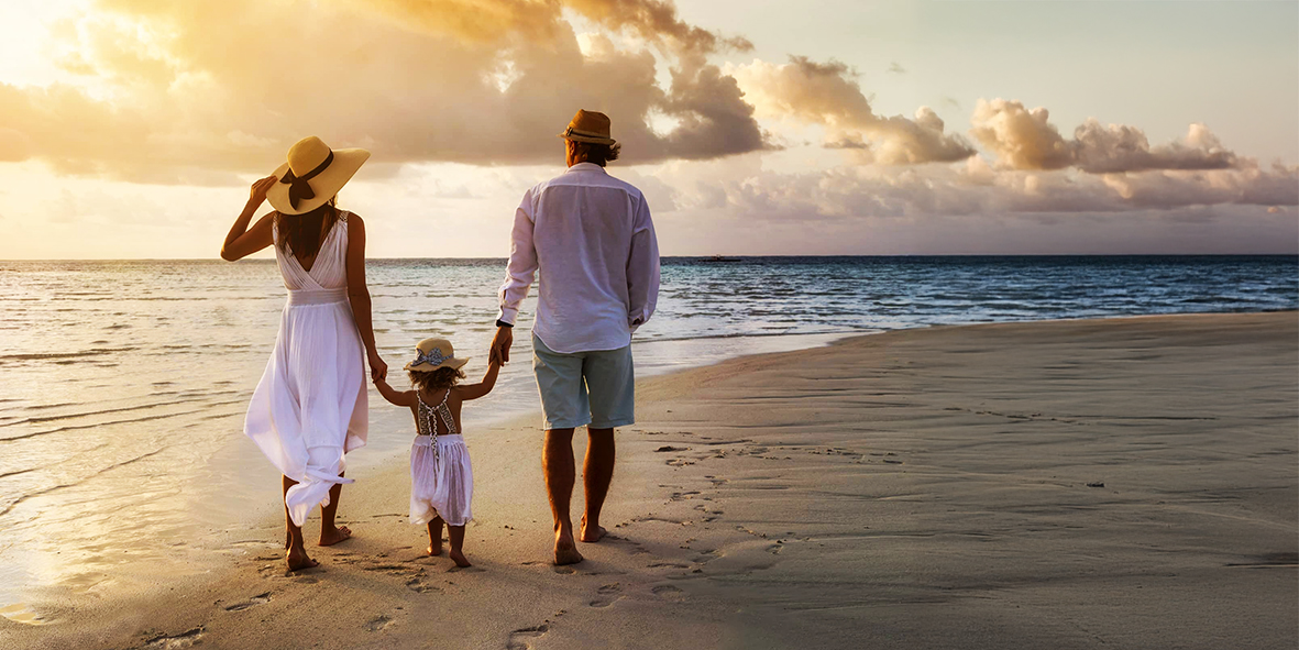 Sesiones de familia Pareja y su hijo pequeño caminando por la playa al atardecer.- Capricolor